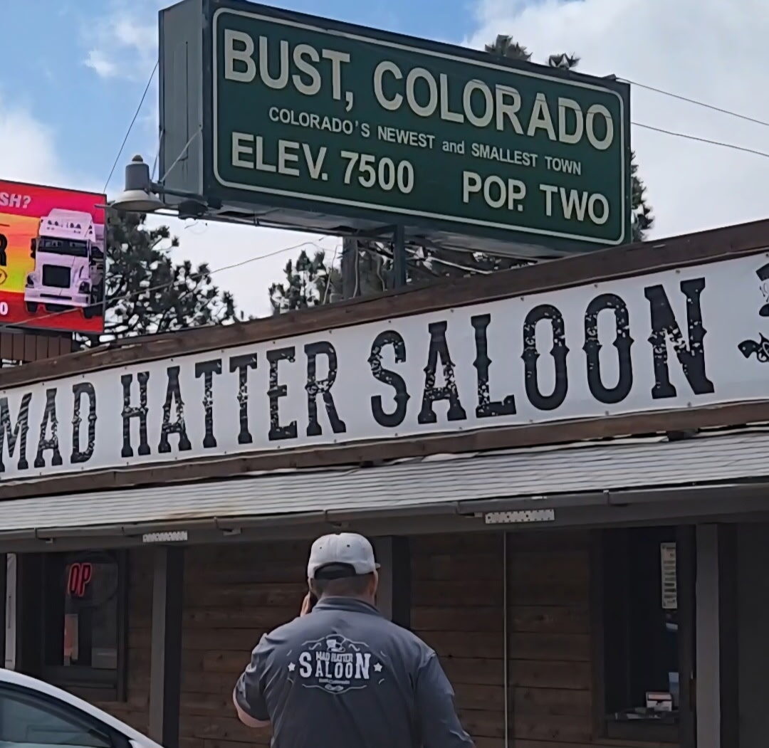 Bust, Colorado sign above The Mad Hatter Saloon's exterior on Highway 24 in Cascade, CO