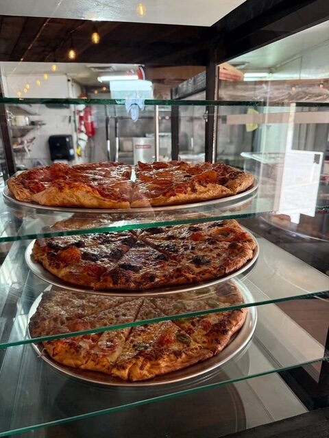 Fresh wood-fired pizzas ready by the slice in the display case at The Mad Hatter Saloon in Cascade, CO